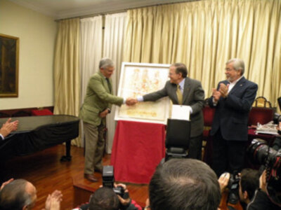 Presentación de un mural en un evento formal, con tres personas intercambiando gestos de respeto y celebración.