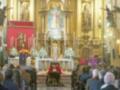 Interior de una iglesia con un altar dorado, estatuas y flores. Personas en trajes formales observan el altar.