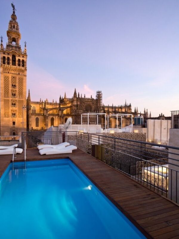 Un hermoso balcón con una piscina azul brillante y sillas de relajación, frente a la icónica Giralda en Sevilla.