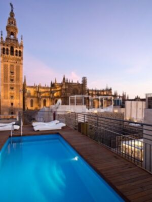 Un hermoso balcón con una piscina azul brillante y sillas de relajación, frente a la icónica Giralda en Sevilla.