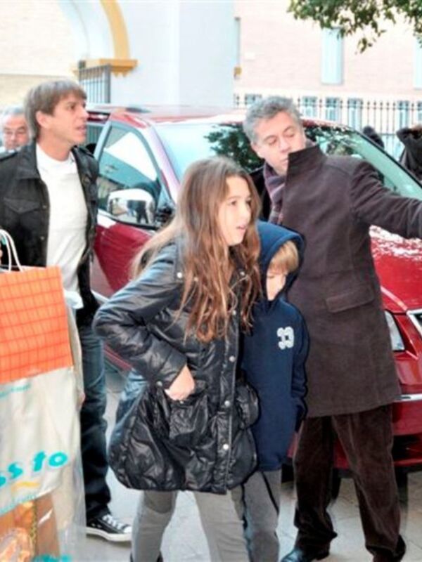 Una familia camina hacia un vehículo rojo, con una niña en medio. La imagen muestra a adultos y niños vestidos de abrigo, caminando por una calle.