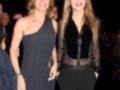 Dos mujeres posan juntas en un evento formal, una con vestido negro y otra con traje de terciopelo.