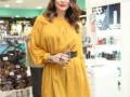 A una mujer con un vestido amarillo brillante, posiblemente en una tienda de belleza o farmacia. El fondo contiene productos cosméticos y publicidad.