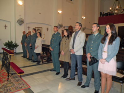 Una imagen de una ceremonia religiosa en un templo, con personas vestidas formalmente y algunos en uniforme militar. La decoración interior incluye una mesa con flores, un púlpito y un altar. La iluminación es suave, creando una atmósfera serena y reverente.