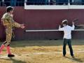Un torero y un niño en un ruedo de toros, con el torero enseñando a manejar el muleta.