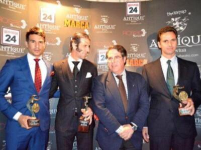 Cuatro hombres en trajes de gala posan con sus premios en una alfombra roja. El fondo es un muro de anuncios con logos y texto en francés.