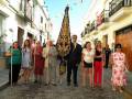 Una procesión religiosa en un pueblo andaluz, con personas vestidas de colores y una figura central con un manto dorado.