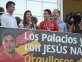 Un grupo de personas, incluyendo a un joven con una camiseta de la selección española, sonríen mientras sostienen una pancarta que dice "Los Palacios y con JESÚS NAVARRO". La imagen se toma en un evento público, posiblemente una celebración o reconocimiento al jugador Jesús Navarro.