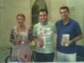 Tres personas sonrientes, dos hombres y una mujer, posando con libros en sus manos. La imagen parece estar tomada en un entorno interior, posiblemente una sala o biblioteca.