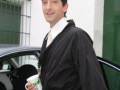 Adrien Brody, actor famoso, posando con una taza de café frente a un coche.