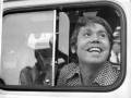 Un hombre sonríe ampliamente mientras mira hacia arriba a través de una ventana de coche. La imagen es en blanco y negro, capturando un momento de felicidad o sorpresa.