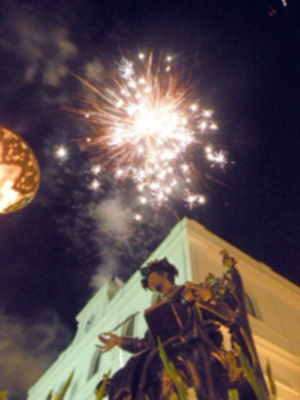 Festividad nocturna con fuegos artificiales y figura en traje medieval en el centro de la imagen.