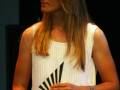 Una mujer con vestido blanco sostiene un premio en forma de abanico en un evento formal.