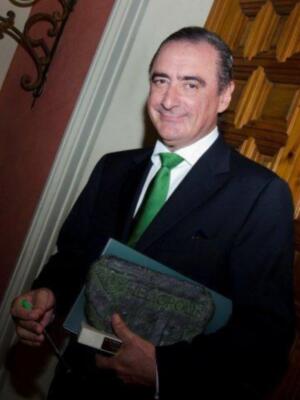 Un hombre con traje y corbata verde sosteniendo un libro.