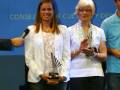Una mujer recibe un premio mientras sonríe y aplaude, con un fondo azul que incluye el texto 'CONSEJERÍA DE CULTURA Y DEPORTE'.