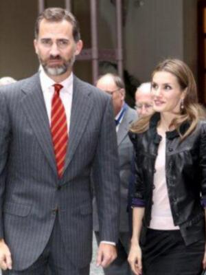 Imagen de un hombre y una mujer caminando juntos. El hombre lleva un traje con corbata roja y la mujer una chaqueta negra. Fondo urbano con edificios modernos.