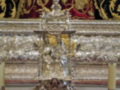 Imagen de un altar con detalles dorados y una figura en el centro, rodeado de velas encendidas y una alfombra roja.