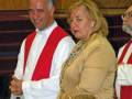 Una imagen de una ceremonia religiosa donde un hombre y una mujer están sonriendo mientras otros participantes observan.