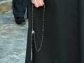Un monje con un largo hábito negro y una cadena de rosario colgando del cuello.