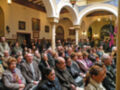 Auditorio lleno de personas en una sala con arcos y decoración vintage.