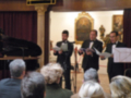 Concierto de música clásica en un salón elegante con orquesta y público atento.