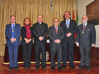 Grupo de personas en trajes formales posando frente a una bandera.