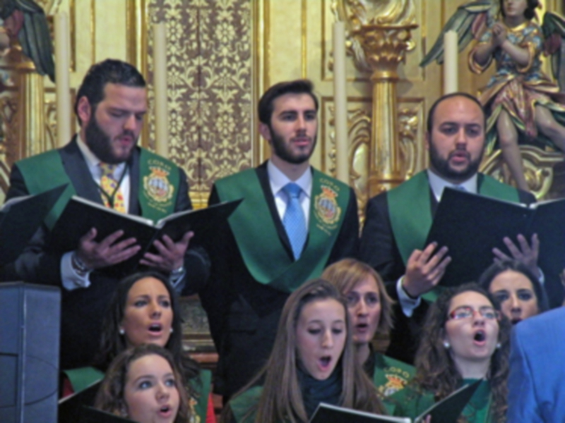 Un coro ejecuta con entusiasmo en un entorno religioso, rodeado de detalles ornamentales y figuras de santos.
