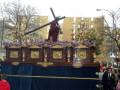 Procesión religiosa con estandarte de Jesús portando la cruz, adornado con detalles dorados y flores, en un entorno urbano.