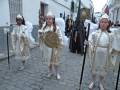Tres niños vestidos con trajes blancos y dorados, posiblemente de un desfile o fiesta religiosa. La imagen muestra detalles como sombreros, plumas y trajes elaborados.
