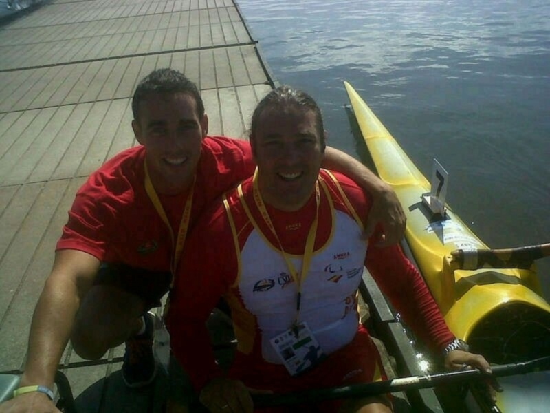 Dos atletas sonrientes en un kayak, listos para competir en una regata de remo paralímpico.