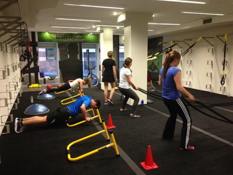 Gente realizando ejercicios de bootcamp en un gimnasio bien equipado con obstáculos y equipos de entrenamiento.