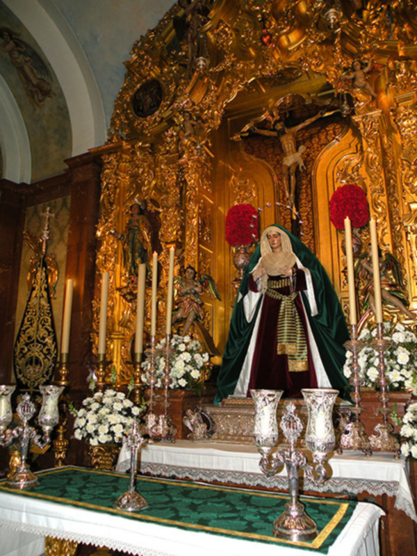 Altar ornado con figuras religiosas y flores rojas y blancas, representando una escena de culto.