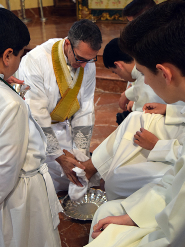 Un sacerdote y jóvenes sacerdotes participan en una ceremonia religiosa, con el sacerdote bendiciendo y colocando un paño sobre uno de los jóvenes.