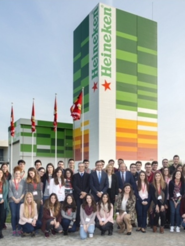 Estudiantes posan frente a la fábrica de Heineken, con banderas y edificio moderno en el fondo.