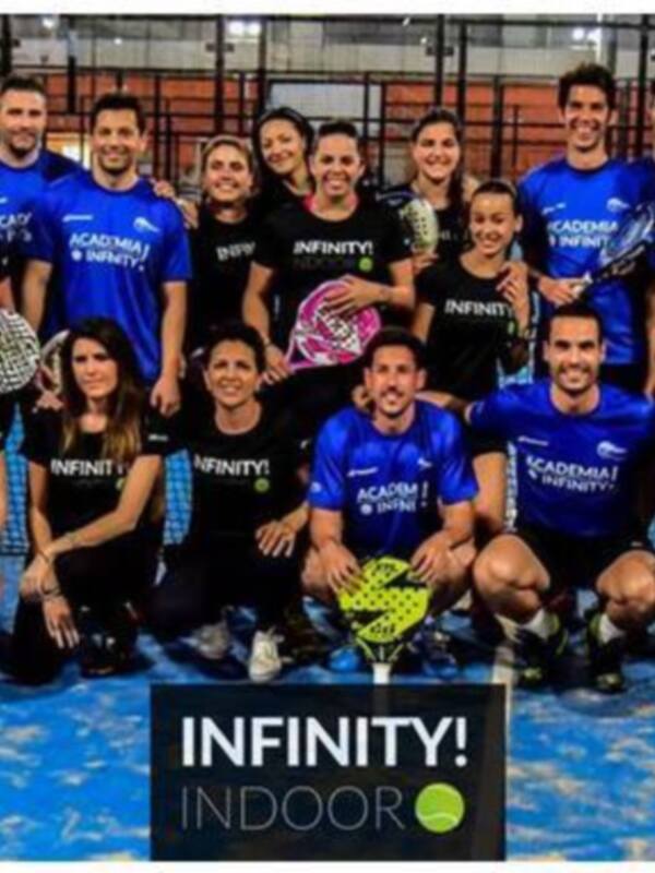 Equipo de padel posando en una cancha de pista azul, con la marca 'INFINITY!' en el fondo y 'ACADEMIA INFINITY!' en la camiseta de algunos miembros.