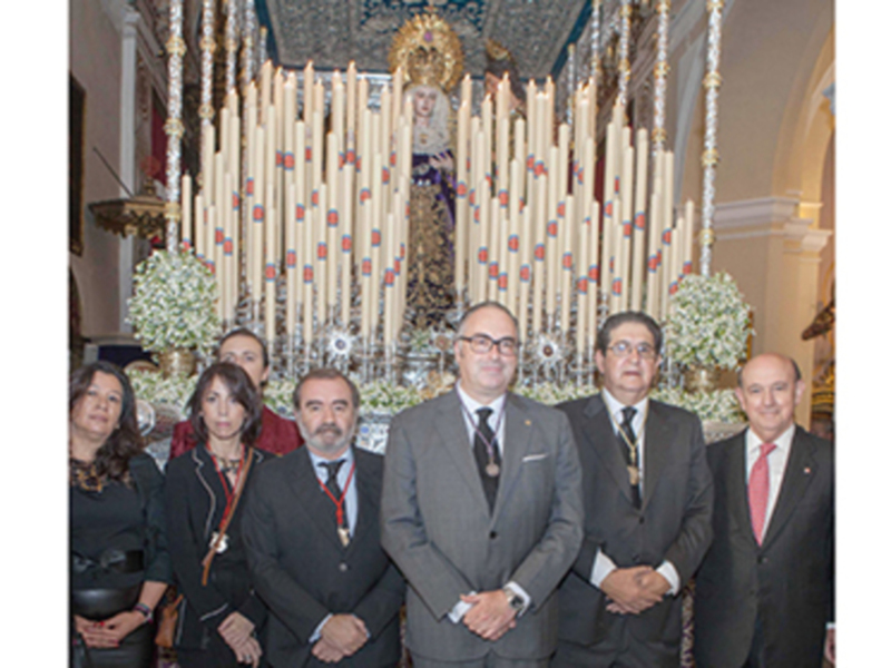 Grupo de personas posando frente a una imagen religiosa en una iglesia, con velas y flores en el fondo.
