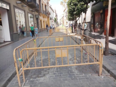 Fotografía de una calle con personas caminando, toldos y carteles.
