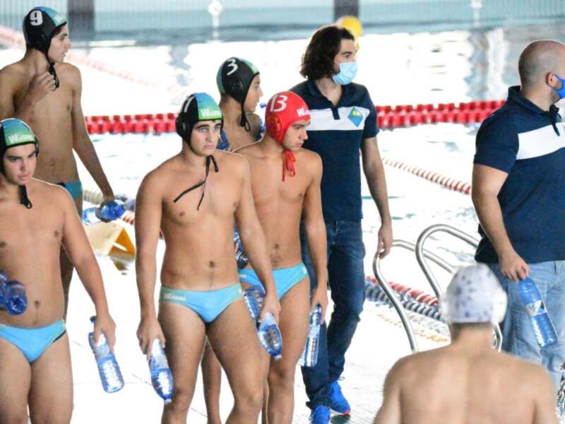 Jóvenes en trajes de baño y cascos de natación en una piscina, posiblemente antes o después del entrenamiento.