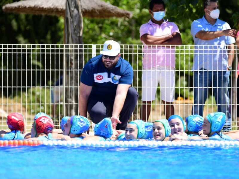 Niños aprendiendo a nadar en una piscina con adultos observando.