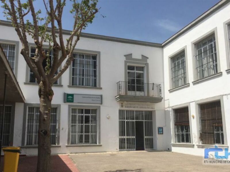 Edificio blanco con ventanas y un árbol en el frente, con un letrero que dice 'Municipio Municipal de Chipiona'.