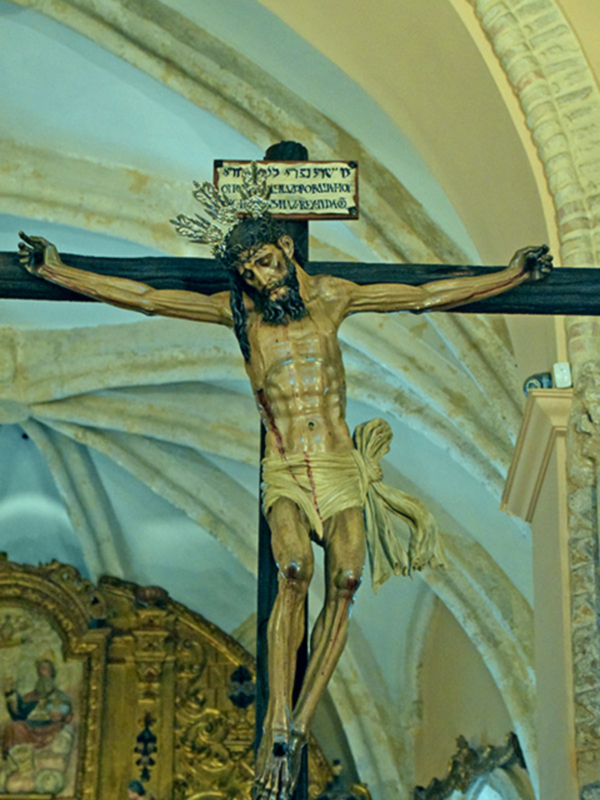 Crucifijo en una iglesia con detalles arquitectónicos y un altar dorado.
