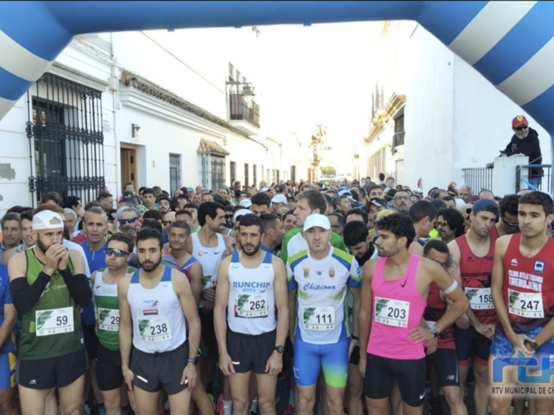 Corredores listos para comenzar una carrera en una calle histórica con edificios blancos y azules al fondo.