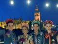 Cuatro jóvenes posan frente a la Giralda de Sevilla, con trajes típicos y un techo azul en el fondo.