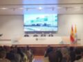 Presentación en la Universidad de San Isidoro, con un panel de tres personas frente a una gran pantalla. La audiencia está sentada en filas, observando atentamente el evento.